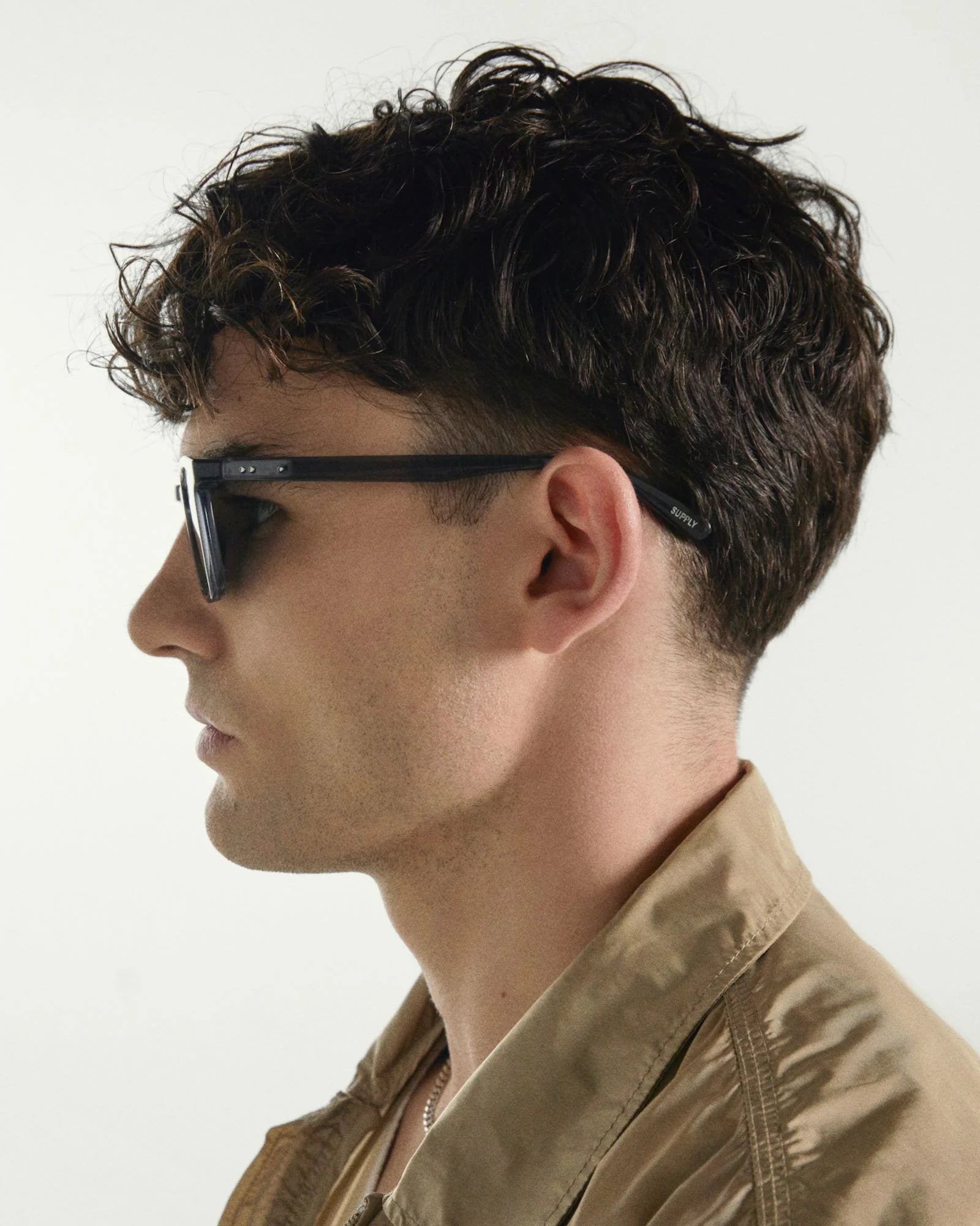 Man wearing sunglasses and a brown jacket against a white background