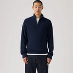 Man wearing a navy blue sweater with a white shirt underneath on a light gray background