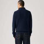 Person wearing a navy sweater and dark jeans on a light gray background