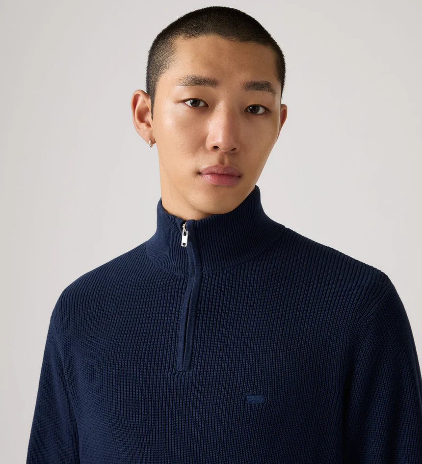 Man wearing a navy blue turtleneck sweater against a plain background