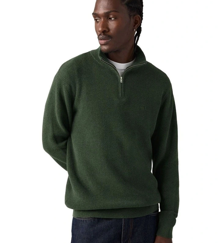 A man wearing a dark green ribbed quarter-zip pullover sweater, paired with dark blue jeans, photographed against a solid white background.