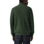 A man viewed from the back wearing a dark green ribbed knit sweater and dark blue jeans against a plain white background.