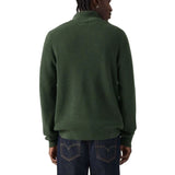 A man viewed from the back wearing a dark green ribbed knit sweater and dark blue jeans against a plain white background.