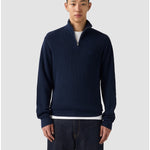 Man wearing a navy blue sweater with a white shirt underneath on a light gray background