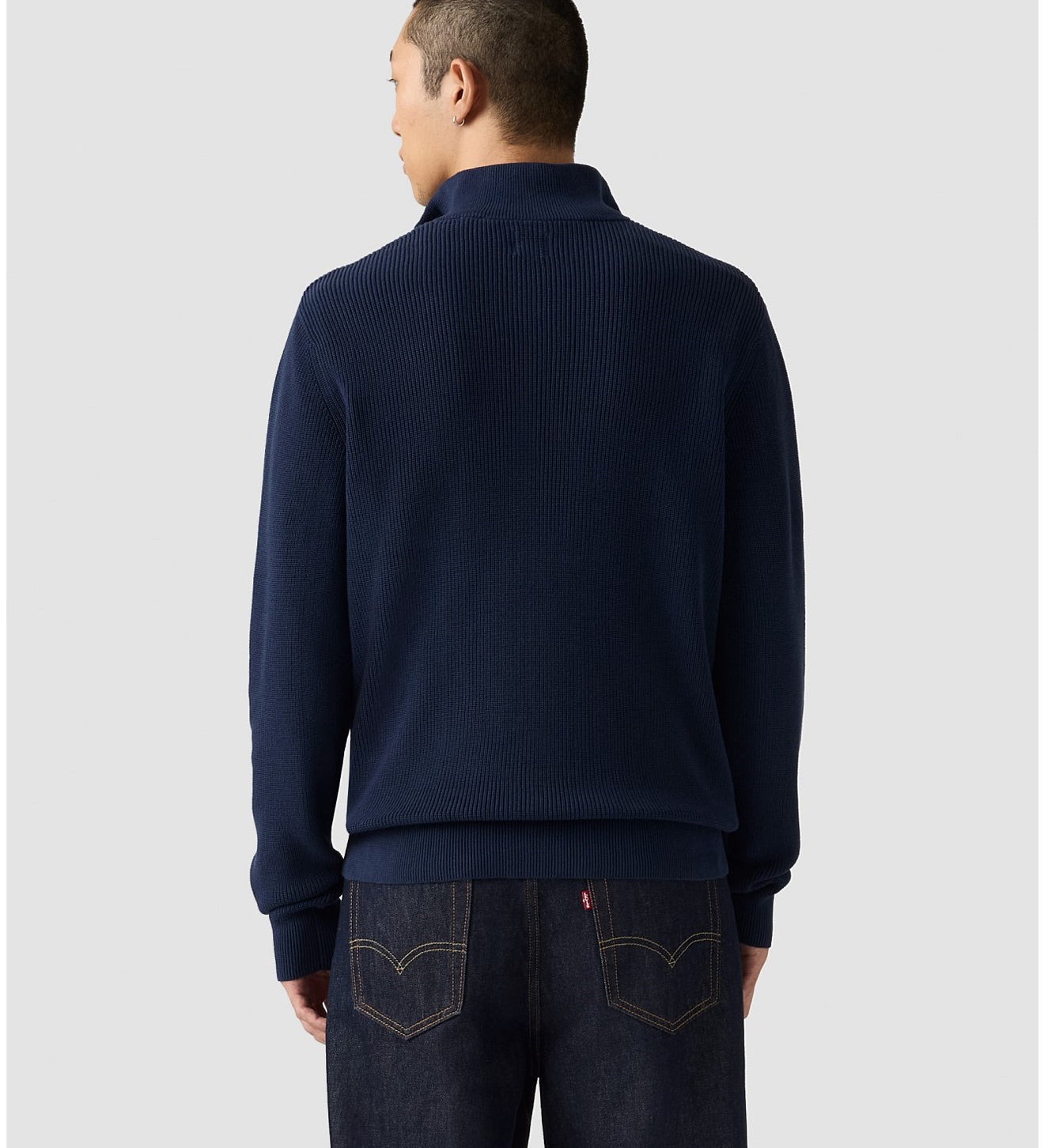 Man wearing a navy blue sweater and jeans on a light gray background