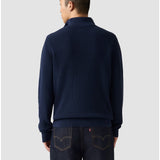 Man wearing a navy blue sweater and jeans on a light gray background