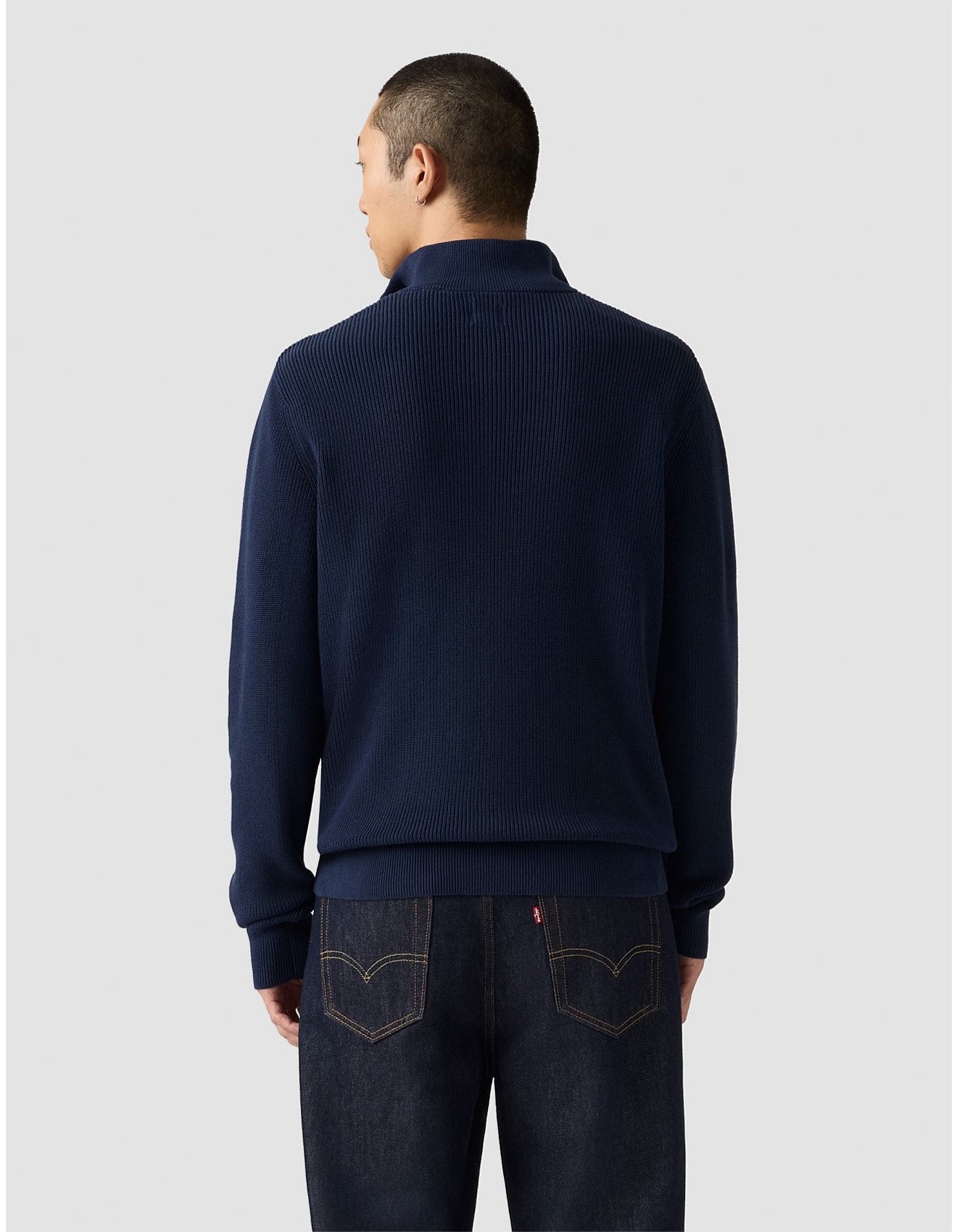 Man wearing a navy blue sweater and jeans on a light gray background