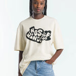 Person wearing a beige t-shirt with text and blue jeans on a white background