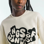 Person wearing a beige sweatshirt with 'Kings of Indigo' text design.