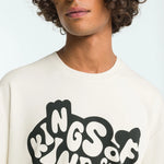 Person wearing a white t-shirt with 'Kings of Kindie' text design on a plain background