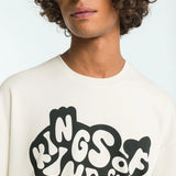 Person wearing a white t-shirt with 'Kings of Kindie' text design on a plain background