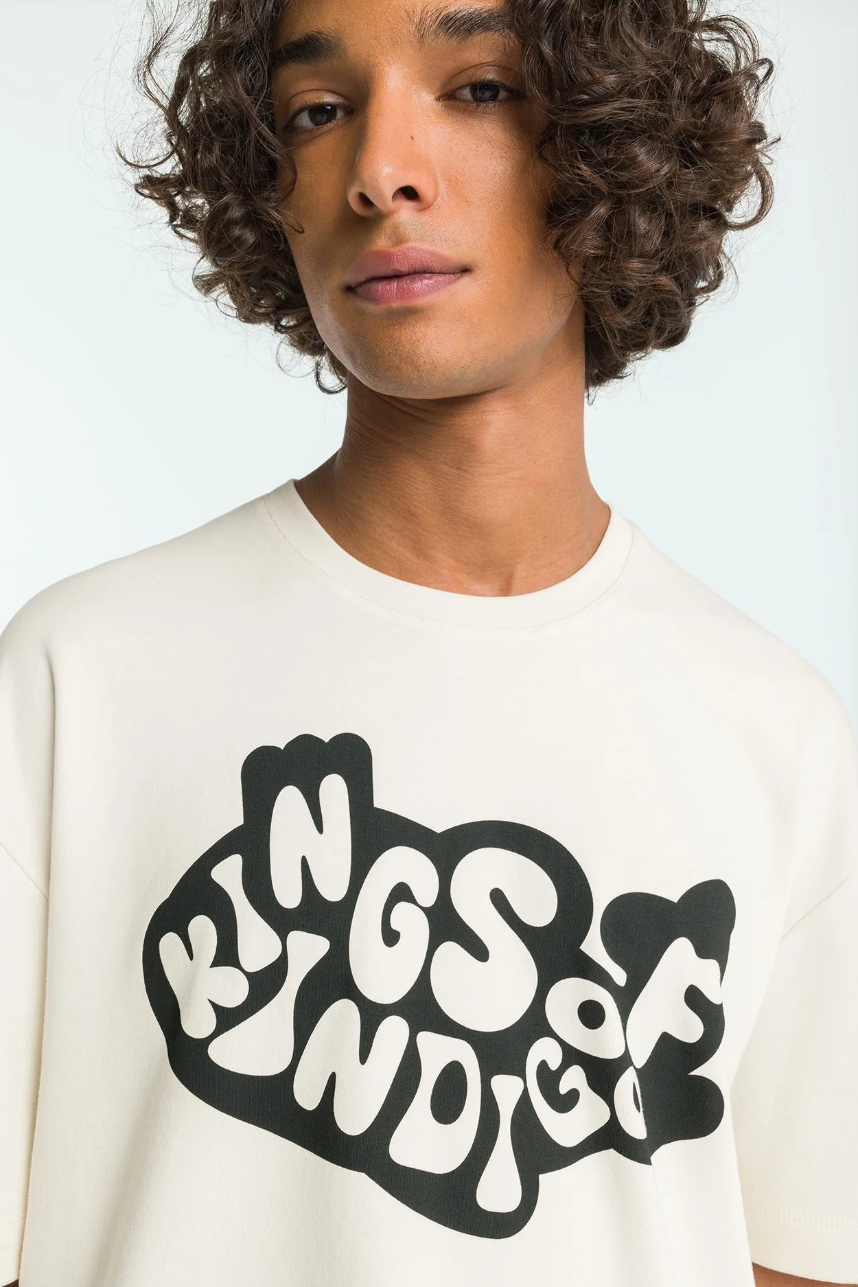 Person wearing a white t-shirt with 'Kings of Kindie' text design on a plain background