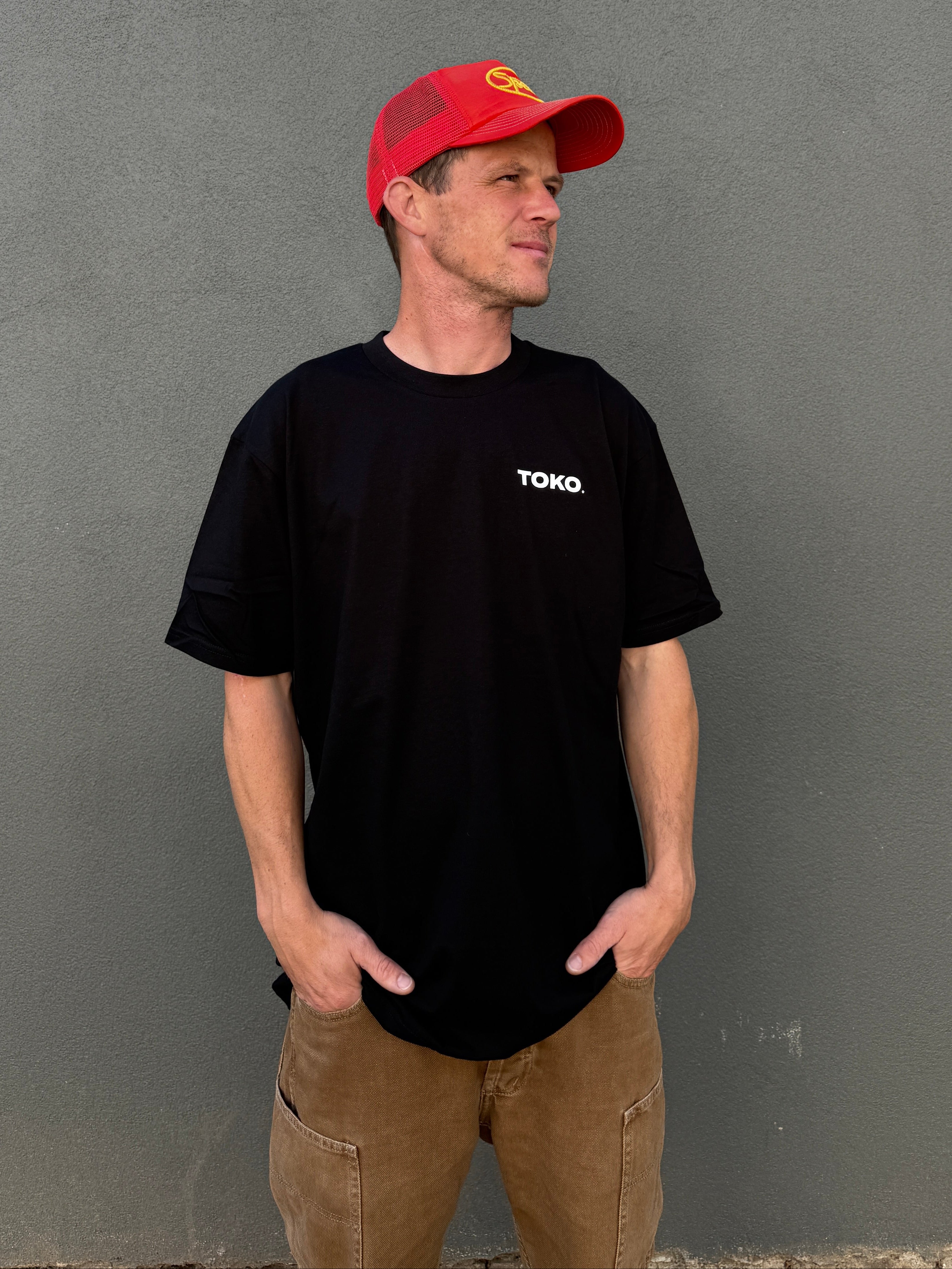 Man wearing a black t-shirt with 'TOKO' logo and a red cap on a gray background