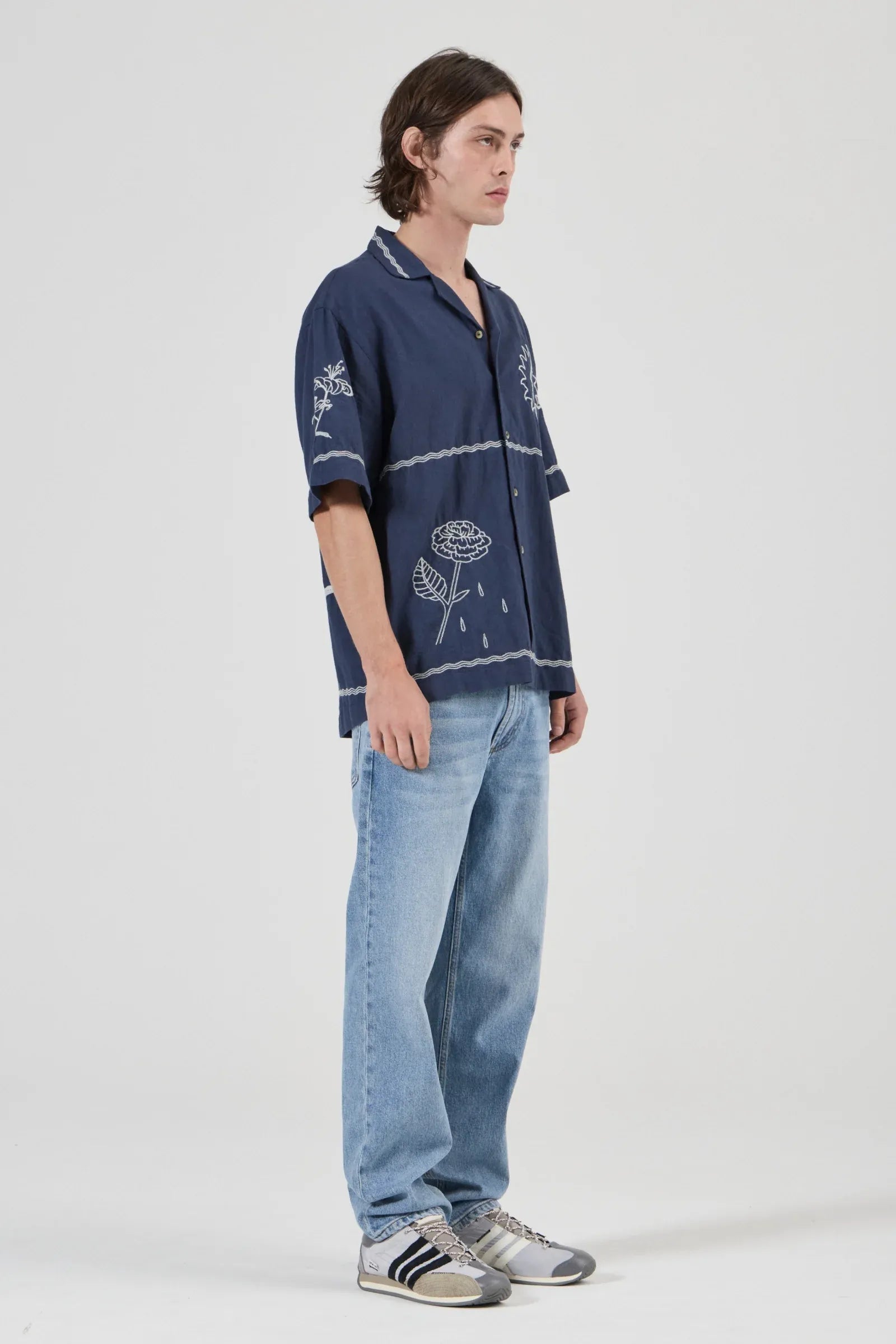 Person wearing a navy blue embroidered shirt and light blue jeans on a white background