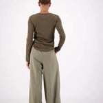 Person wearing a green long-sleeve top and wide-leg pants on a white background