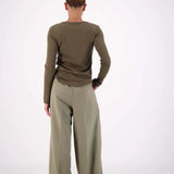 Person wearing a green long-sleeve top and wide-leg pants on a white background