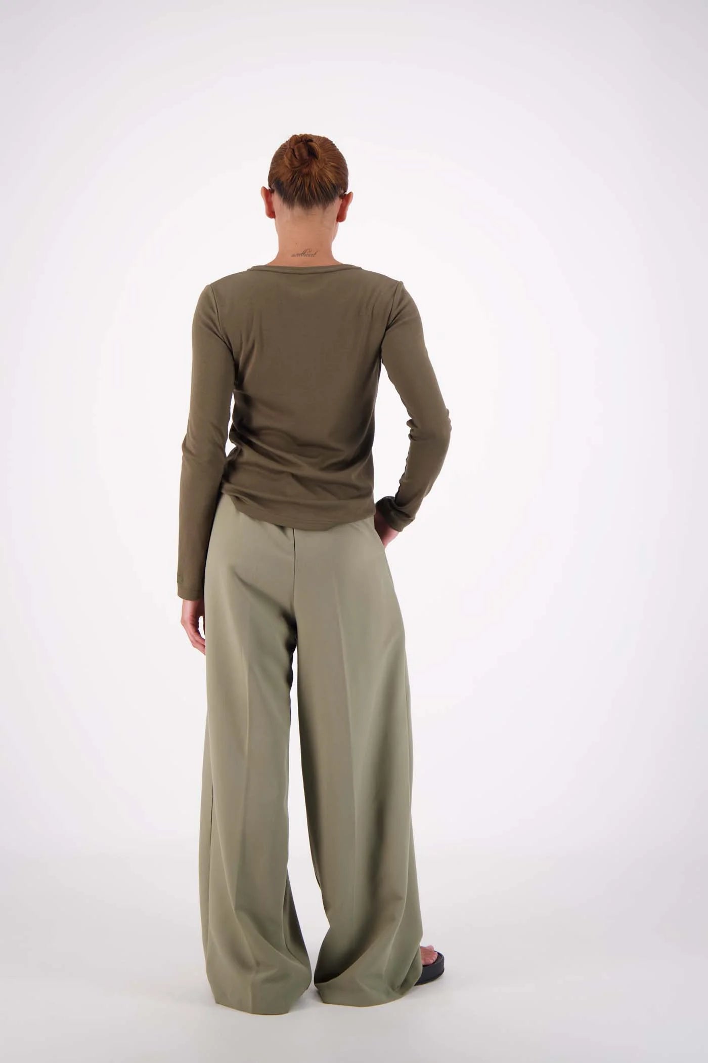 Person wearing a green long-sleeve top and wide-leg pants on a white background