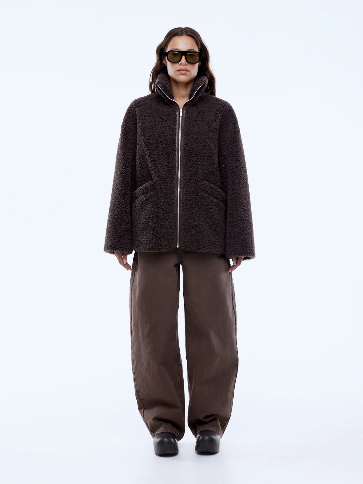 Person wearing a brown jacket and pants on a white background