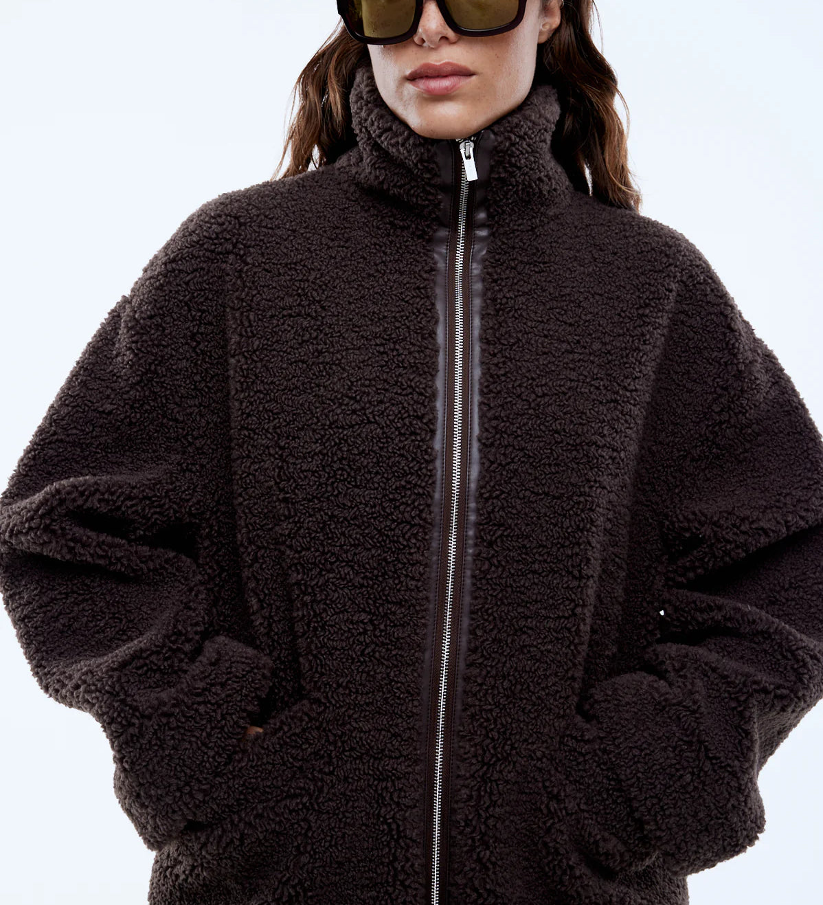 Person wearing a dark brown fleece jacket and sunglasses on a light gray background