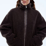 Person wearing a dark brown fleece jacket and sunglasses on a light gray background