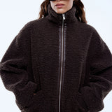 Person wearing a dark brown fleece jacket and sunglasses on a light gray background