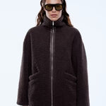 Person wearing a dark brown jacket and sunglasses on a light blue background