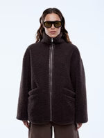 Person wearing a dark brown jacket and sunglasses on a light blue background