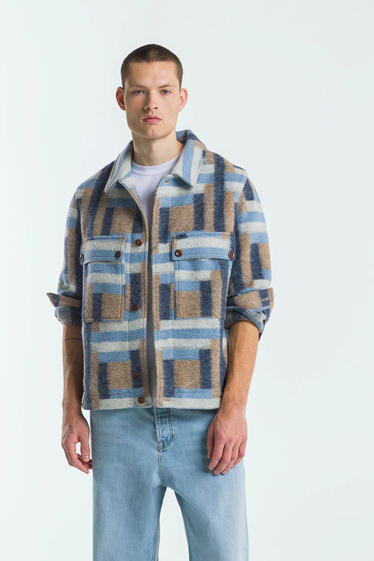 Man wearing a plaid shirt over a white t-shirt with light blue jeans on a white background
