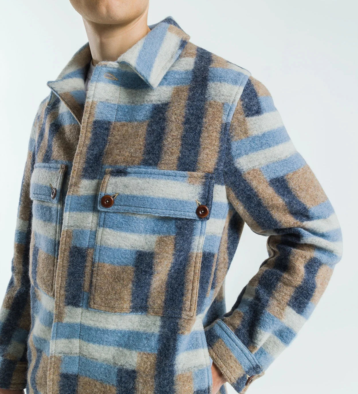 Person wearing a plaid shirt with blue, brown, and beige pattern on a white background