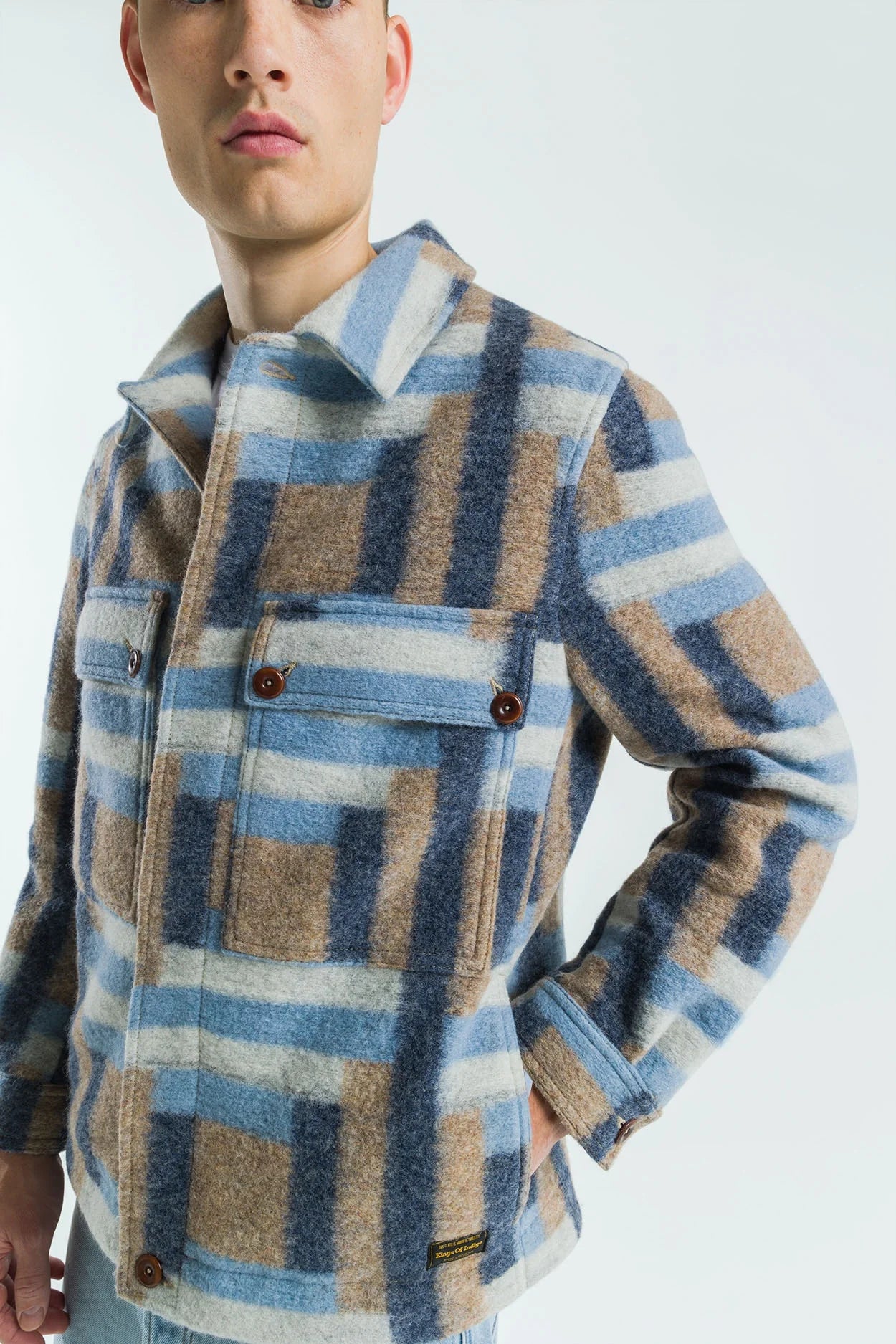 Person wearing a plaid shirt with blue, brown, and beige pattern on a white background
