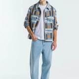 Man wearing a plaid shirt over a white t-shirt with light blue jeans on a white background