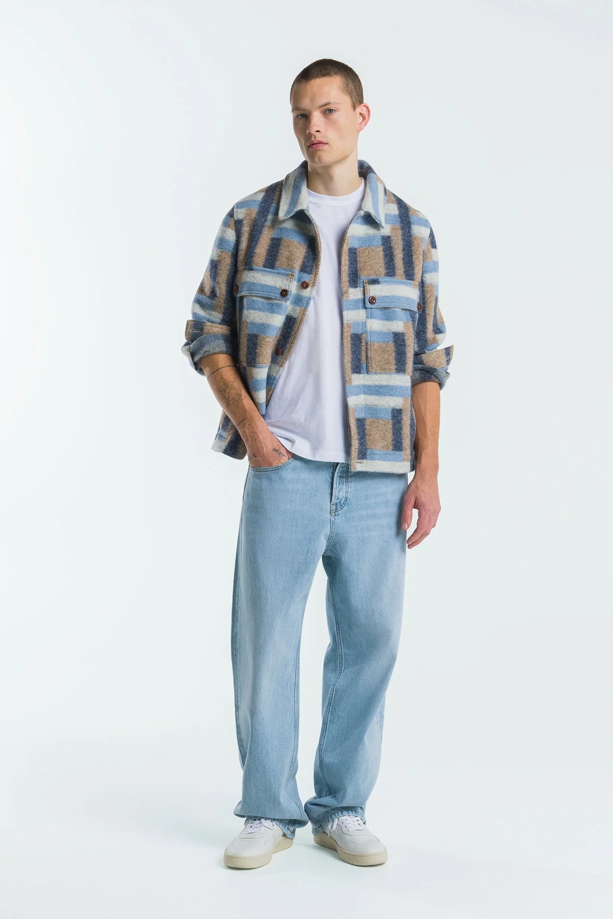 Man wearing a plaid shirt over a white t-shirt with light blue jeans on a white background