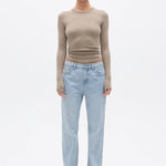 Woman wearing a beige long-sleeve top and light blue jeans on a white background