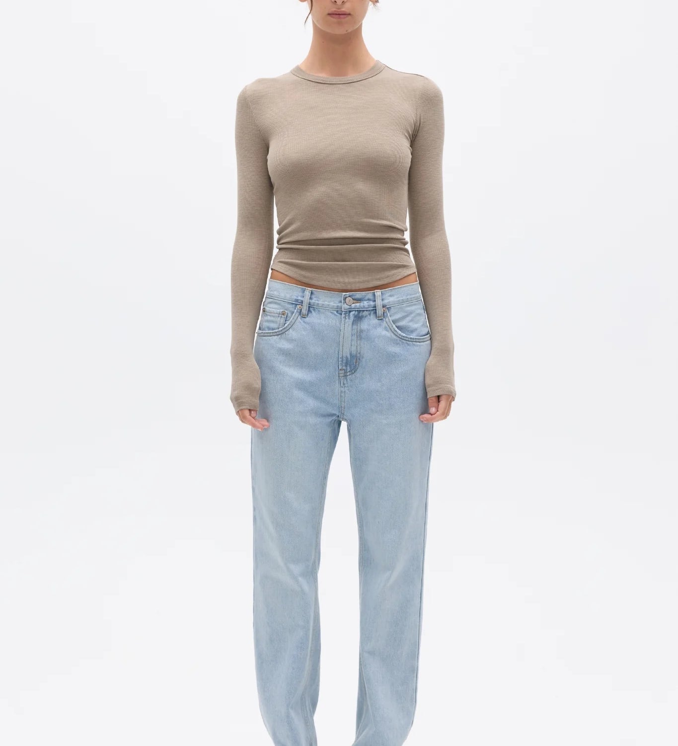 Woman wearing a beige long-sleeve top and light blue jeans on a white background