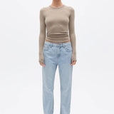Woman wearing a beige long-sleeve top and light blue jeans on a white background