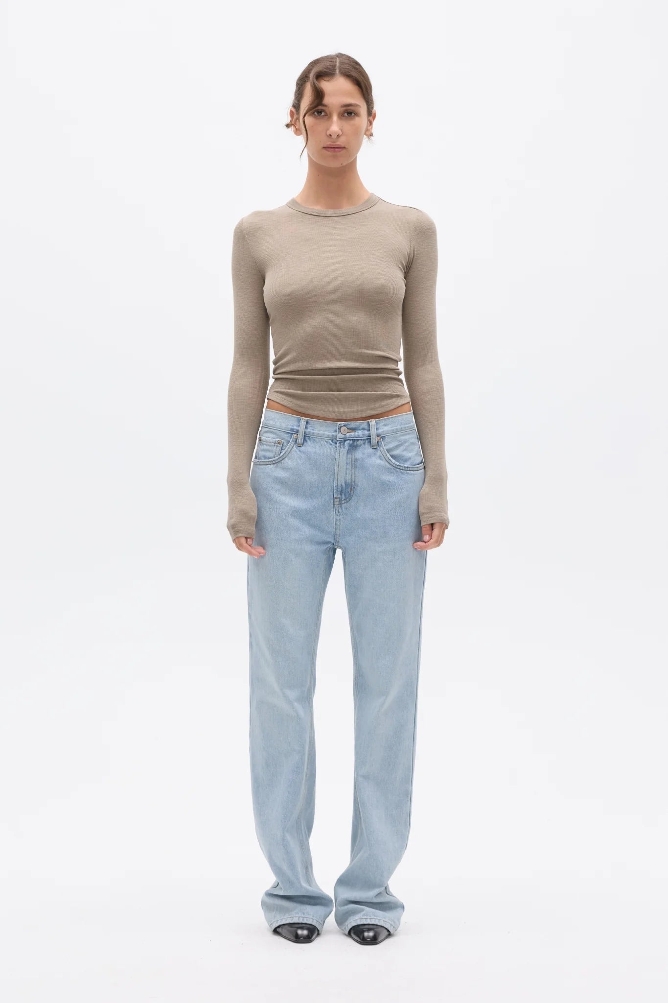 Woman wearing a beige long-sleeve top and light blue jeans on a white background