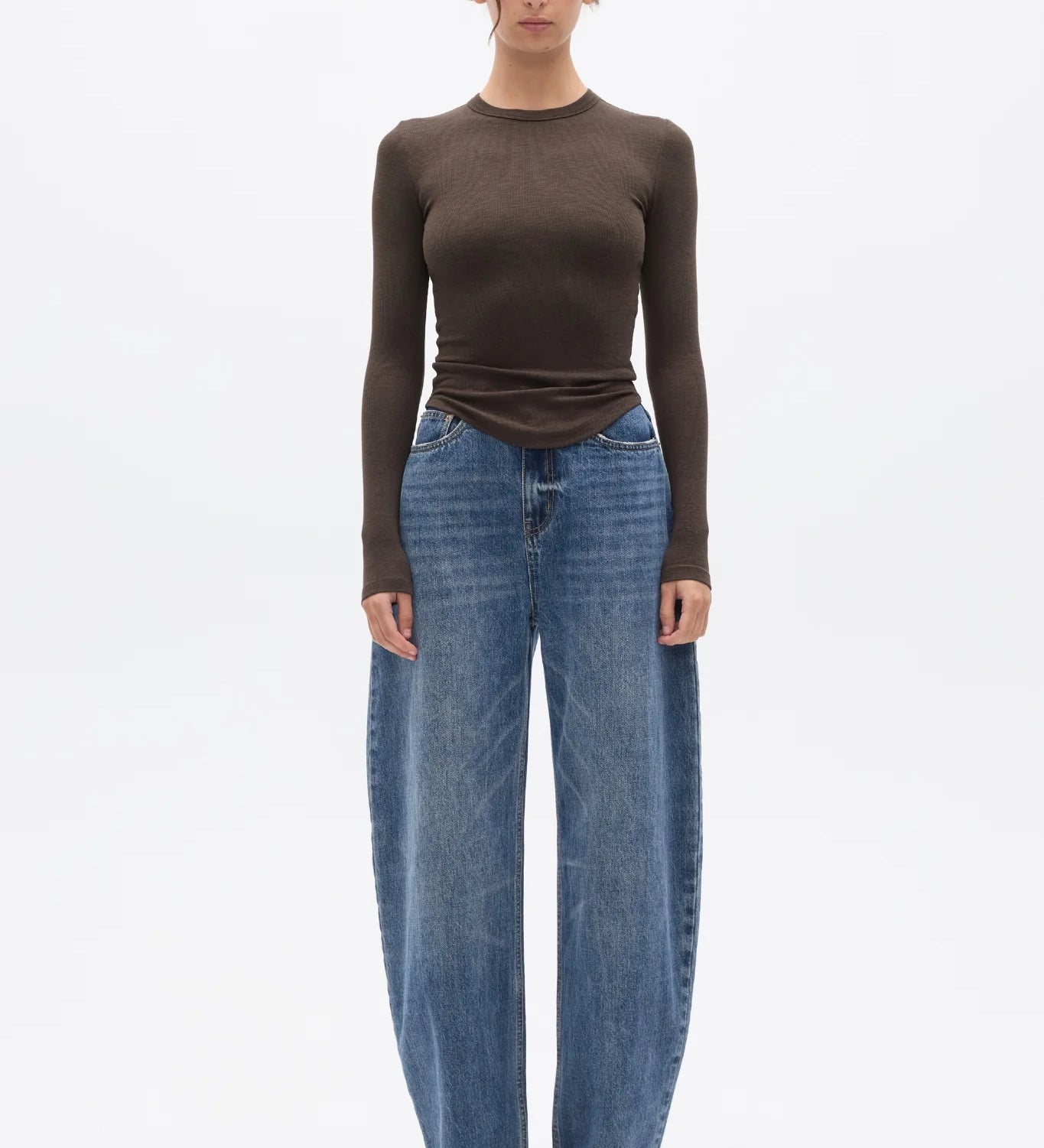 Woman wearing a brown long-sleeve top and blue jeans on a white background