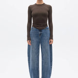 Woman wearing a brown long-sleeve top and blue jeans on a white background