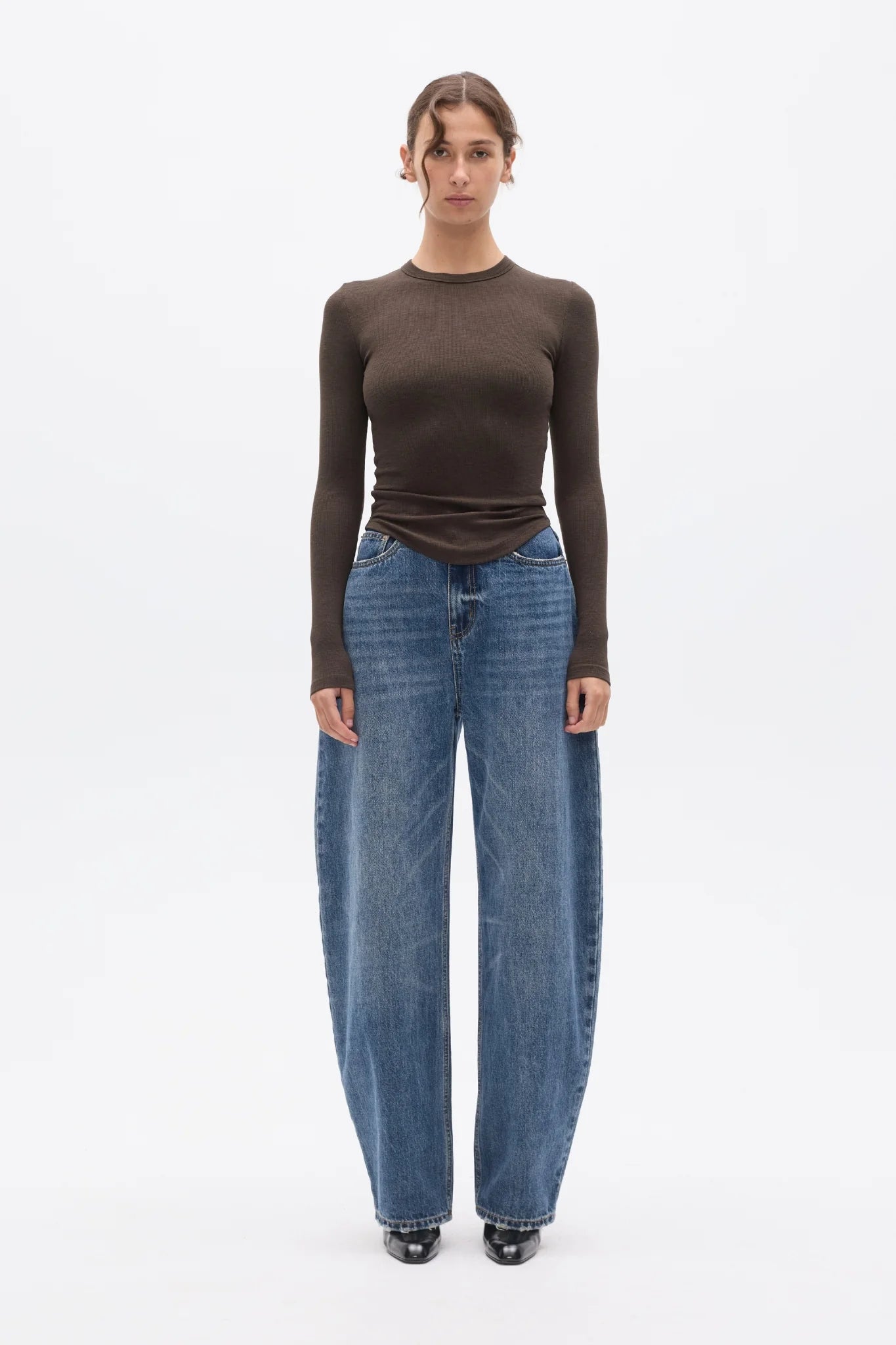 Woman wearing a brown long-sleeve top and blue jeans on a white background