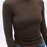 Person wearing a brown long-sleeve top and blue jeans on a white background