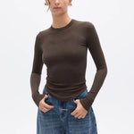 Woman wearing a brown long-sleeve top and blue jeans on a white background