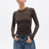 Woman wearing a brown long-sleeve top and blue jeans on a white background