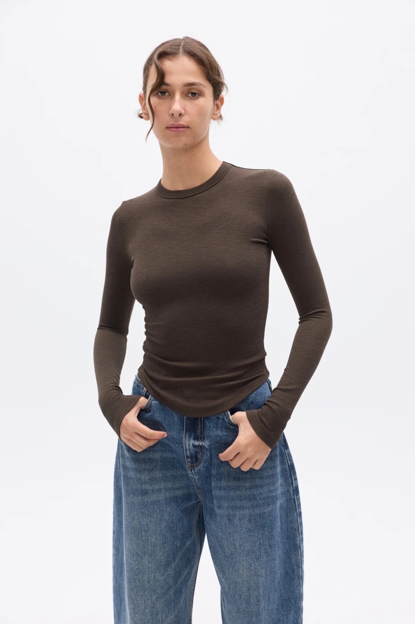 Woman wearing a brown long-sleeve top and blue jeans on a white background