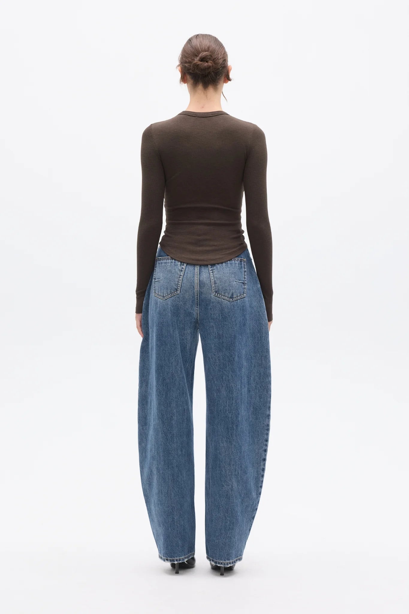 Person wearing a brown long-sleeve top and blue jeans from behind on a white background