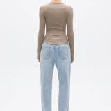 Person wearing a beige long-sleeve top and light blue jeans on a white background