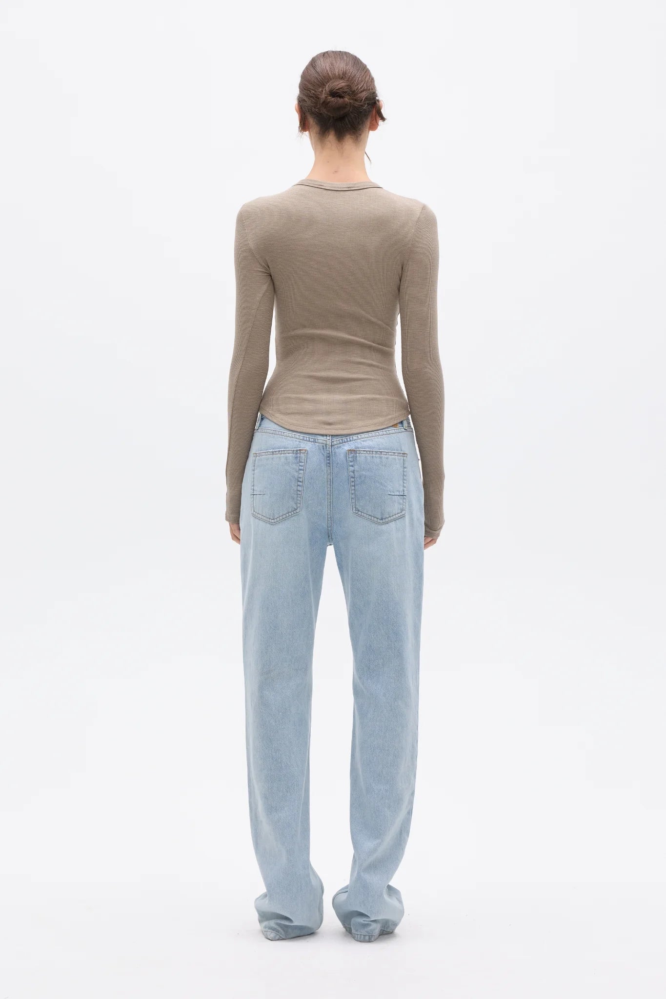 Person wearing a beige long-sleeve top and light blue jeans on a white background