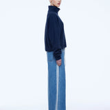 A model shown in profile wearing a dark navy blue mock-neck knit sweater and wide-leg blue denim jeans with white side stripes, against a plain white studio background.