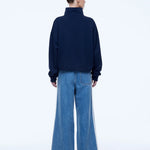A model shown from the back wearing a dark navy blue mock-neck sweatshirt and wide-leg blue denim jeans with white side stripes, against a plain white studio background.
