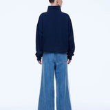 A model shown from the back wearing a dark navy blue mock-neck sweatshirt and wide-leg blue denim jeans with white side stripes, against a plain white studio background.