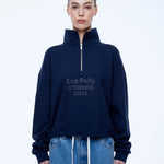 A model wearing a navy blue half-zip sweatshirt with 'Ena Pelly STUDIOS 2014' printed on the chest, paired with light blue denim jeans, against a plain white studio background.